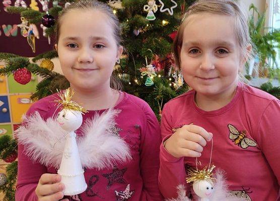 Uczennice stoją przy choince i prezentują aniołki