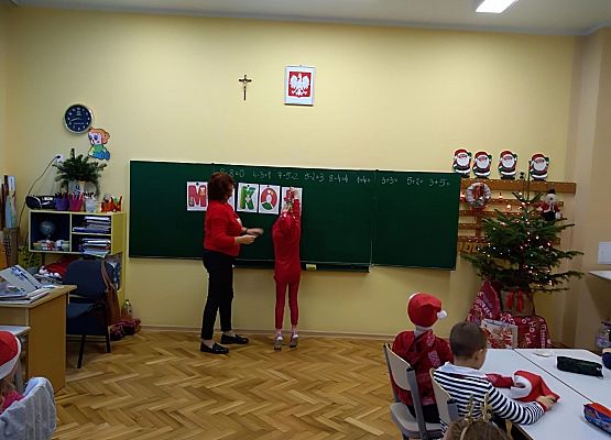Dziecko zawiesza litery na tablicy, obok stoi nauczycielka