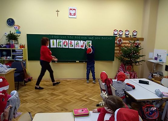 Dziecko zawiesza litery na tablicy, obok stoi nauczycielka