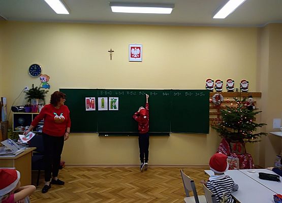 Dziecko zawiesza litery na tablicy, obok stoi nauczycielka