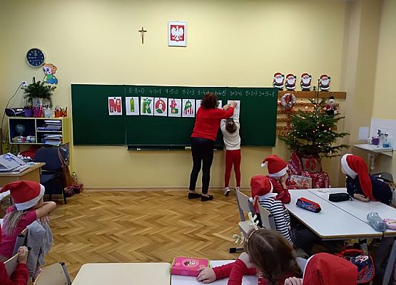 Dziecko zawiesza litery na tablicy, obok stoi nauczycielka