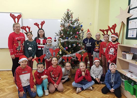Uczniowie i nauczycielka ubrani w mikołajkowe stroje stoją przy choince