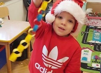 Dziecko w ubraniu świątecznym pokazuje łańcuch choinkowy