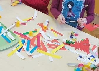 Dwie dziewczynki w świątecznych strojach wykonują łańcuch choinkowy