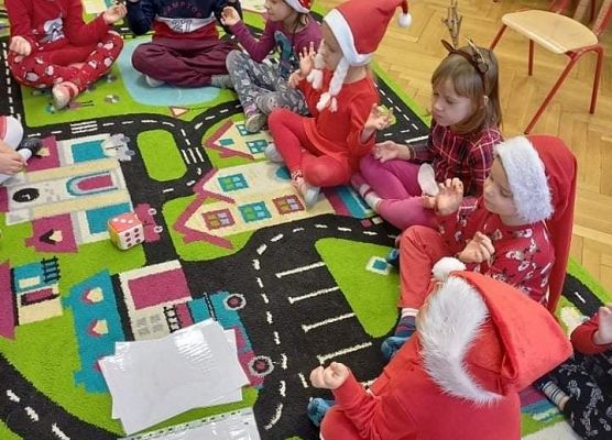 Grupa dzieci w świątecznych strojach siedzi na dywanie