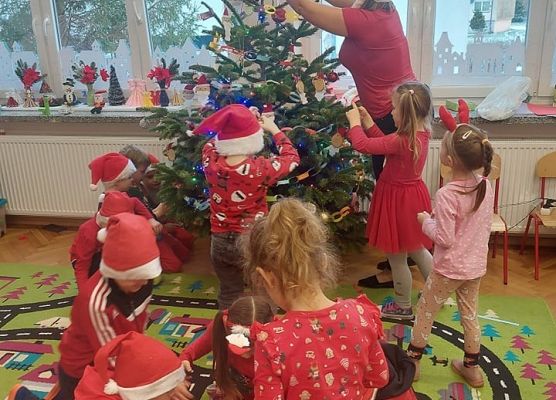 dzieci wraz z nauczycielką ubierają choinkę
