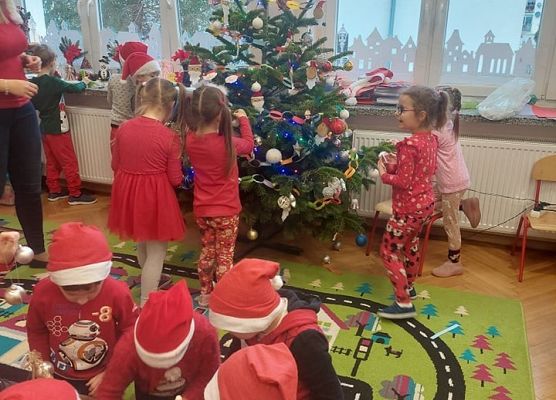 dzieci wraz z nauczycielką ubierają choinkę