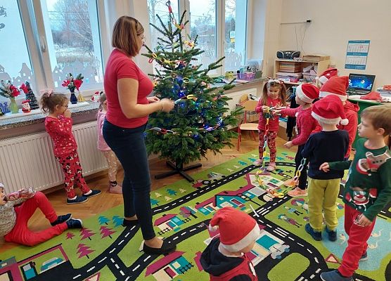 dzieci wraz z nauczycielką ubierają choinkę
