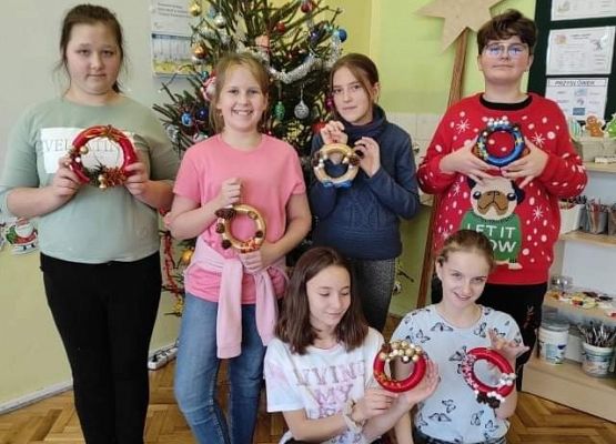 Uczniowie stoją przy choince i prezentują swoje świąteczne prace