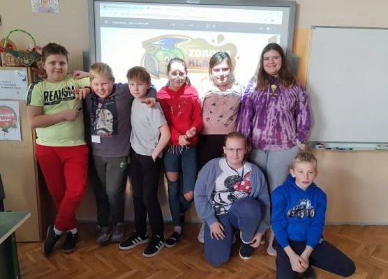 Uczniowie stoją przy tablicy, w tle logo projektu