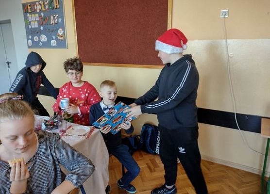 Uczeń w czapce mikołajkowej rozdaje prezenty