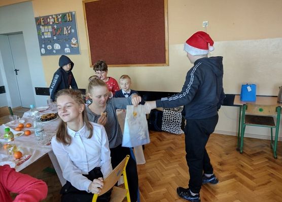 Uczeń w czapce mikołajkowej rozdaje prezenty