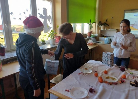 Uczeń w czapce mikołajkowej rozdaje prezenty