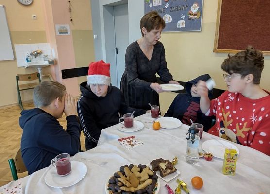 Uczniowie siedzą a nauczycielka rozdaje opłatek