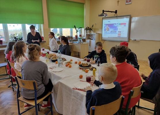 Uczniowie siedzą przy wigilijnym stole. Nauczycielka składa uczniom życznia.