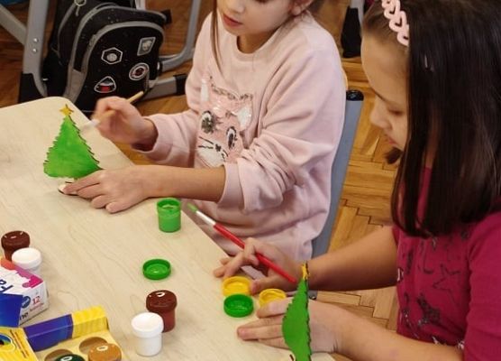 Uczennice malują drewnianą choinkę