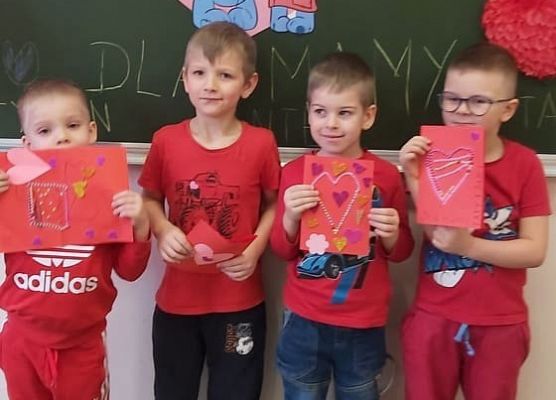 Chłopcy stoją przy tablicy i prezentują walentynkowe kartki