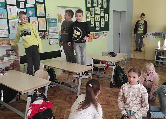 Uczniowie stoją na krzesłach i obserwują emocje innych z różnych pozycji.