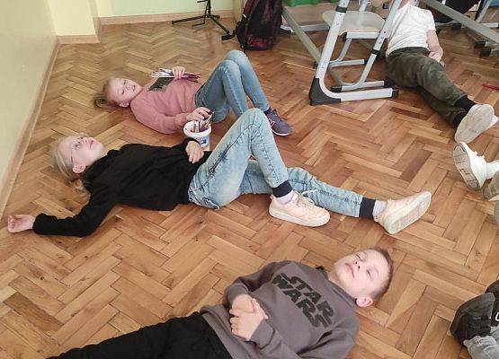 Uczniowie leżą na podłodze i obserwują emocje innych z różnych pozycji