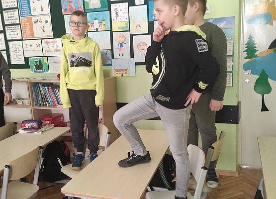 Uczniowie stoją na krzesłach i obserwują emocje innych z różnych pozycji.