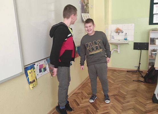 Uczniowie stoją przy tablicy i odgrywają scenkę