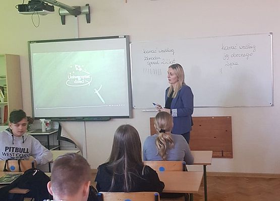 Uczniowie siedzą w ławkach i prowadzą dyskusję