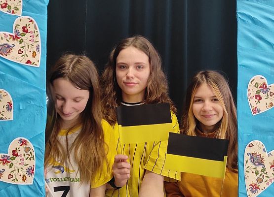 Uczennice stoją w ramce, na której są wzory kaszubskie.