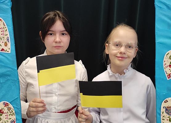 Uczennice stoją w ramce, na której są wzory kaszubskie.