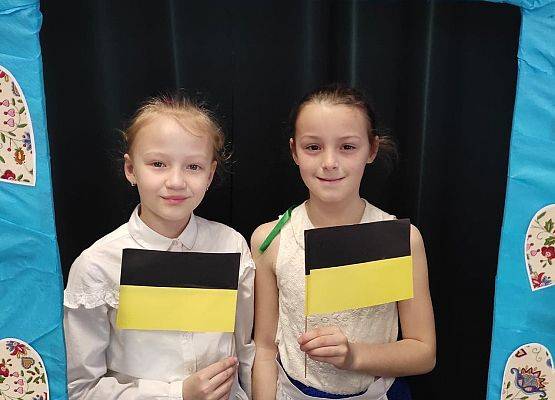 Uczennice stoją w ramce, na której są wzory kaszubskie.