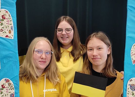 Uczennice stoją w ramce, na której są wzory kaszubskie.