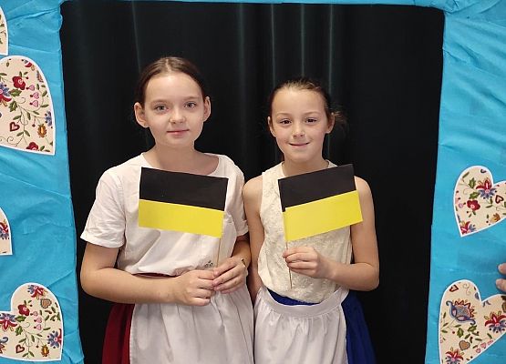 Uczennice stoją w ramce, na której są wzory kaszubskie.