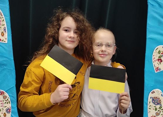 Uczennice stoją w ramce, na której są wzory kaszubskie.