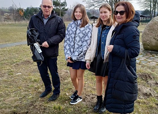 Dyrektor trzyma sadzonkę obok stoją dwie uczennice i nauczycielka