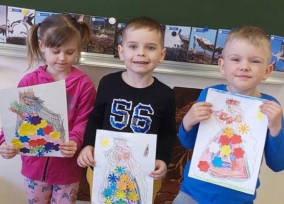 Dzieci stoją przy tablicy i pokazują swoje rysunki
