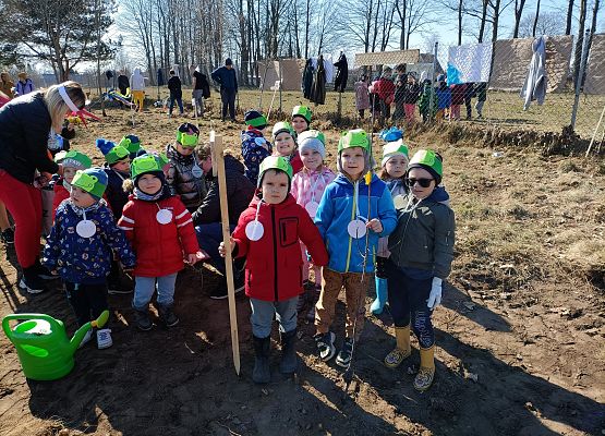 Dzieci stoją w grupie i trzymają tabliczkę z nazwą drzewka owocowego