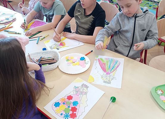 Dzieci siedzą przy stoliku i wykonują pracę plastyczną