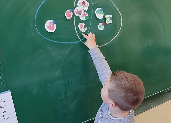 Chłopiec stoi przy tablicy i  pokazuje część wspólną zbioru