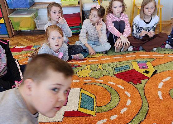Uczniowie siedzą na podłodze i słuchają nauczycielki