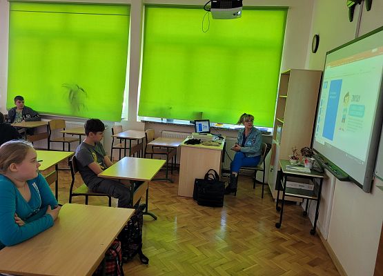 Uczniowie siedzą w ławkach i oglądają prezentację multimedialną