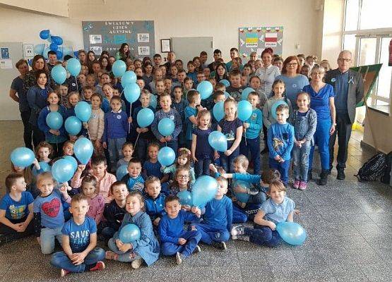 Zdjęcie grupowe przedszkolaków i nauczycieli. Wszyscy w niebieskich ubraniach trzymają niebieskie balony.