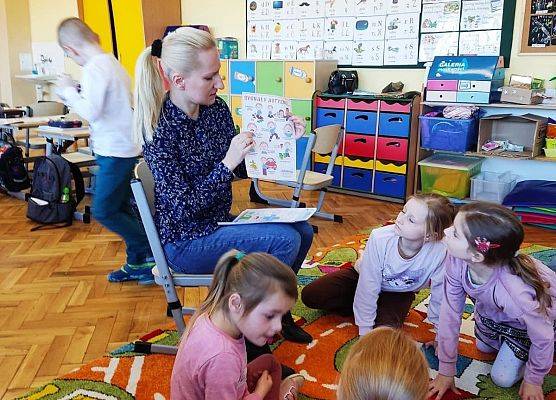 Uczniowie siedzą na dywanie i słuchają nauczycielki