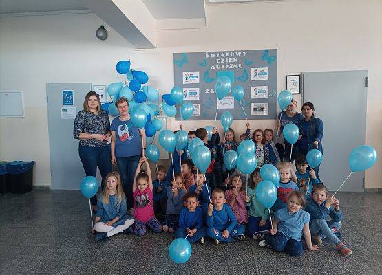 Zdjęcie grupowe przedszkolaków, nauczycielek i opiekunek. Wszyscy ubrani na niebiesko trzymają w dłoniach niebieskie balony.