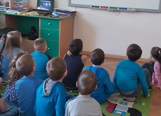 Uczniowie siedzą na dywanie i oglądają film