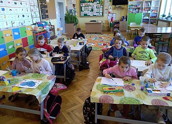 Uczniowie siedzą w ławkach i malują obrazki