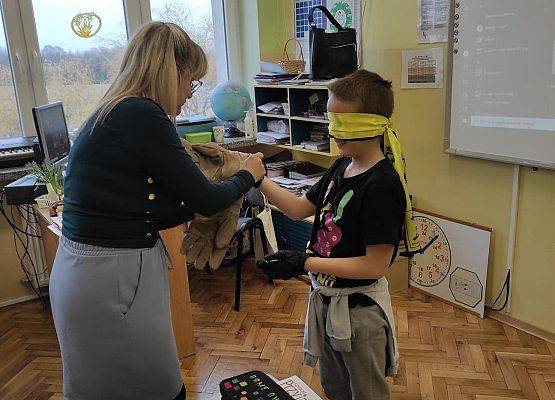 Nauczycielka zakłada rękawice chłopcu z zasłoniętymi oczami