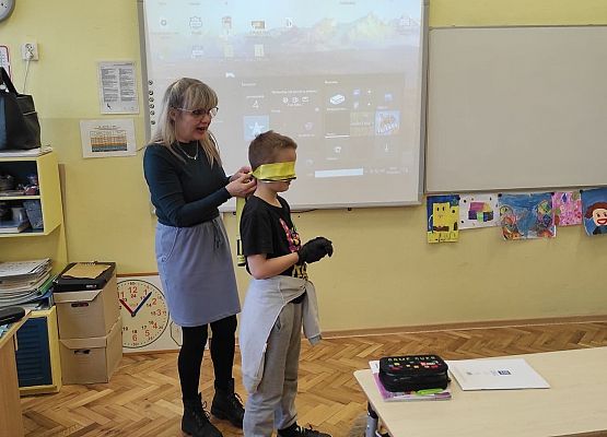 Nauczycielka zakłada uczniowi opaskę na oczy