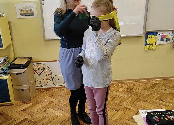 Nauczycielka zakłada uczennicy opaskę na oczy