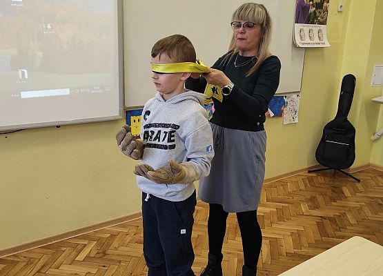 Nauczycielka zakłada uczniowi opaskę na oczy