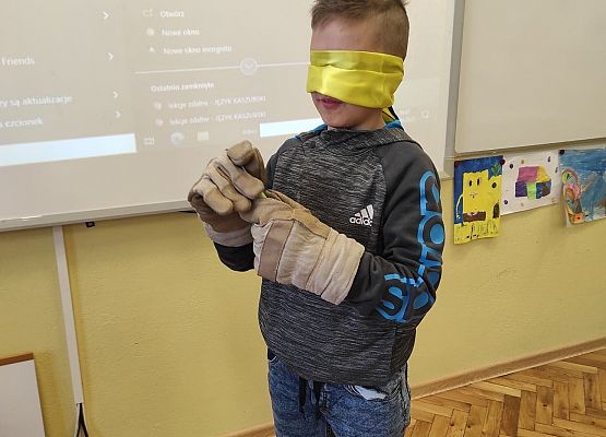 Chłopiec z opaską na oczach ma na dłoniach robocze rękawice