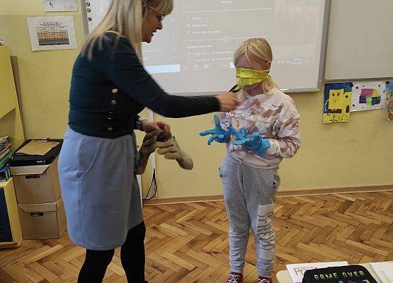 Nauczycielka podaje dziewczynce przedmiot. dziewczynka ma na dłoniach gumowe rękawiczki i zasłonięte oczy
